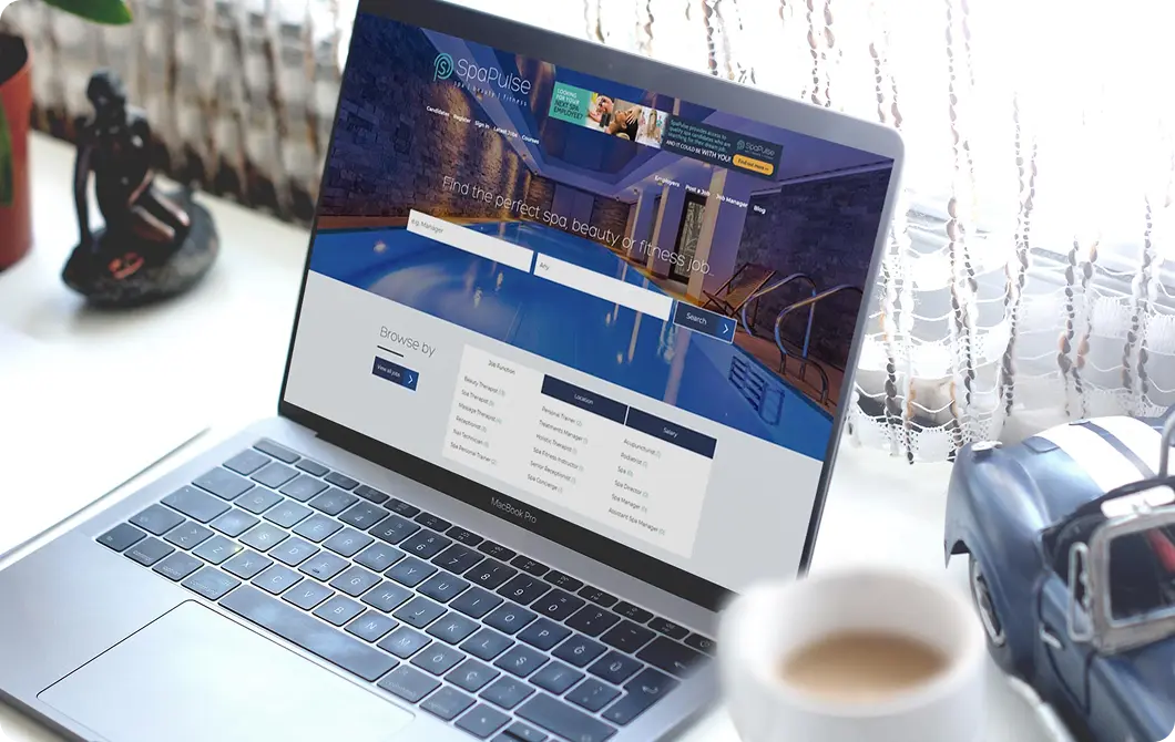 Website displayed on a laptop on a desk with a plant and coffee cup